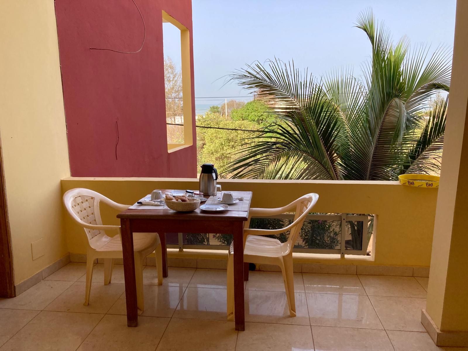 Balcon commun des chambres : table de petit-déjeuner, palmiers et mer à l'horizon